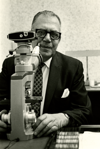 Black and white photo of Julian H. Lewis seated at a microscope.