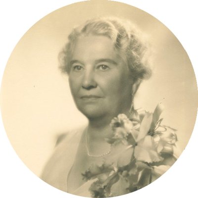 Black-and-white formal photographic portrait of Elizabeth Foss Wilson, circa 1930s. She has short, curly, white hair and is wearing a light colored dress with a large corsage on her left shoulder.